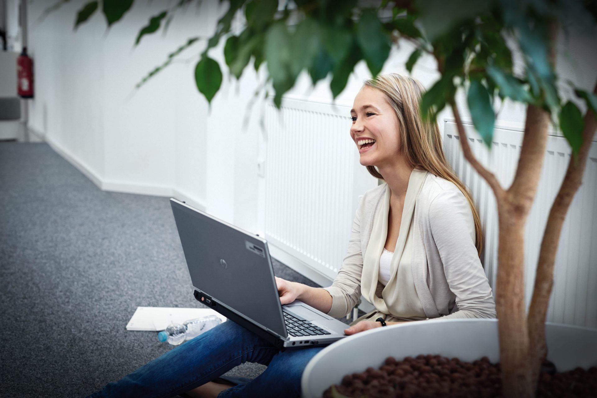 Eine junge Auszubildende der BMW Group sitzt lachend mit ihrem LapTop auf dem Boden.