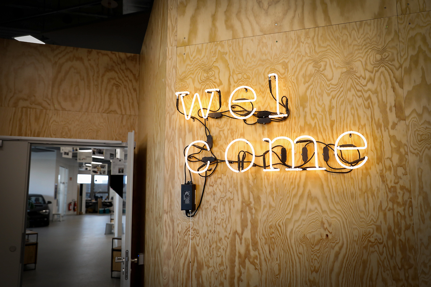 The picture shows the word "Welcome" in neon letters on a wooden wall.