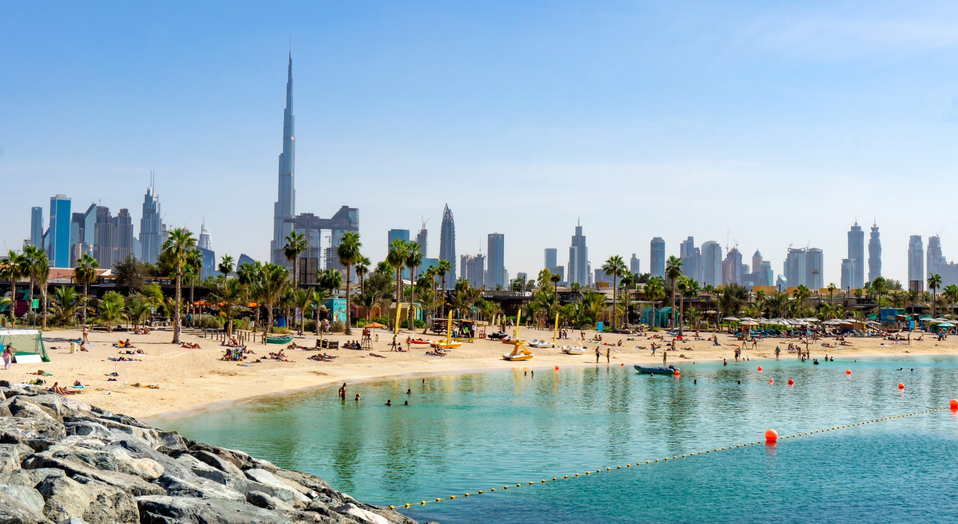 Beach in Dubai with people and skyscapers in the background on a sunny day
