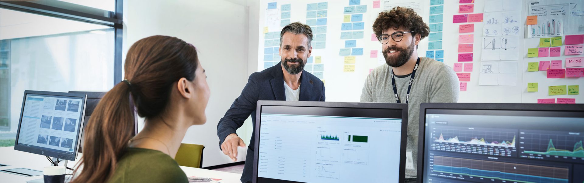 The picture shows three BMW professionals working IT jobs, meeting in an office to discuss a new project. 