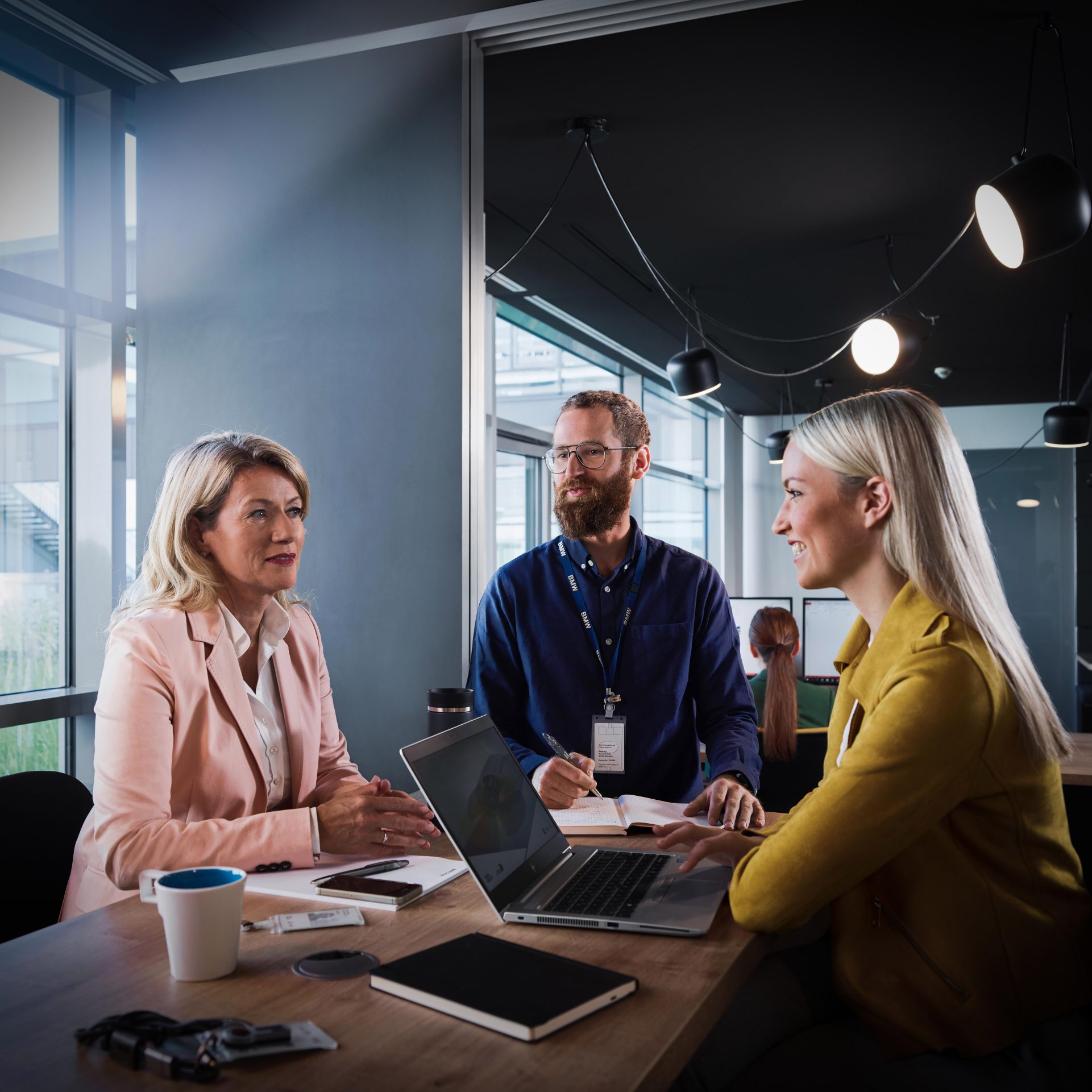 The image shows three BMW Group employees having a meeting.