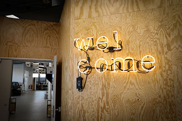 The picture shows the neon sign “welcome” hanging on a wall at the Innovation Lab in Munich.