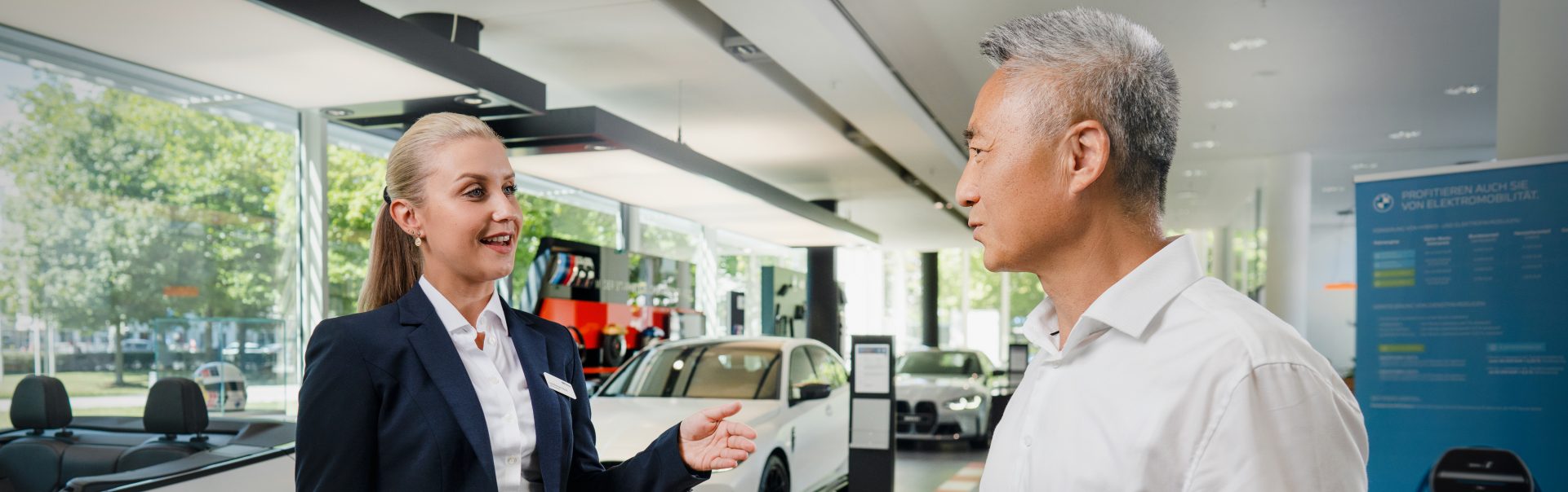 A Car Sales Management Assistant talks to a customer at a BMW dealership.