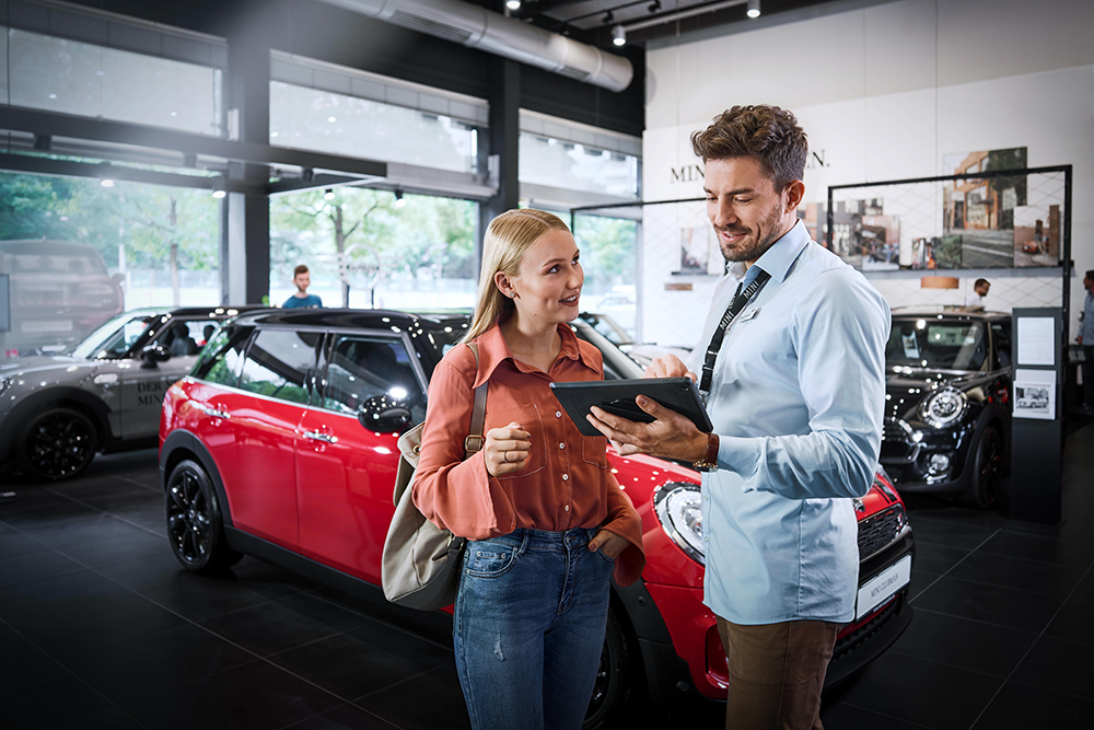 A Car Sales Management Assistant talks to a customer at a BMW dealership.