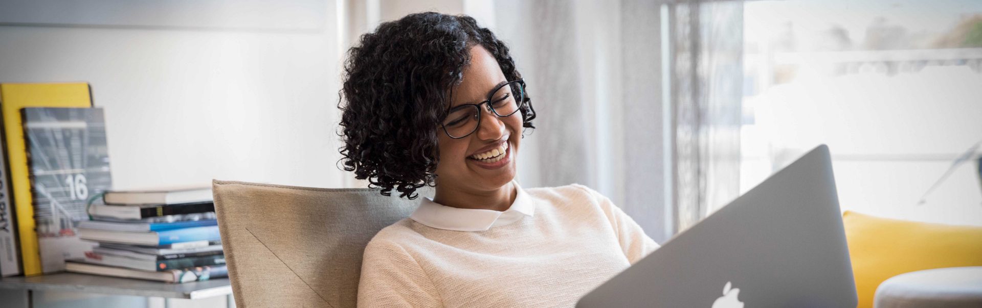 The picture shows a woman using her laptop and laughing.