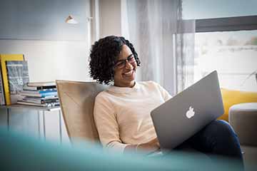 The picture shows a woman using her laptop and laughing.