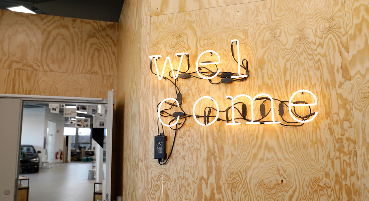 The picture shows the neon sign “welcome” hanging on a wall at the Innovation Lab in Munich.