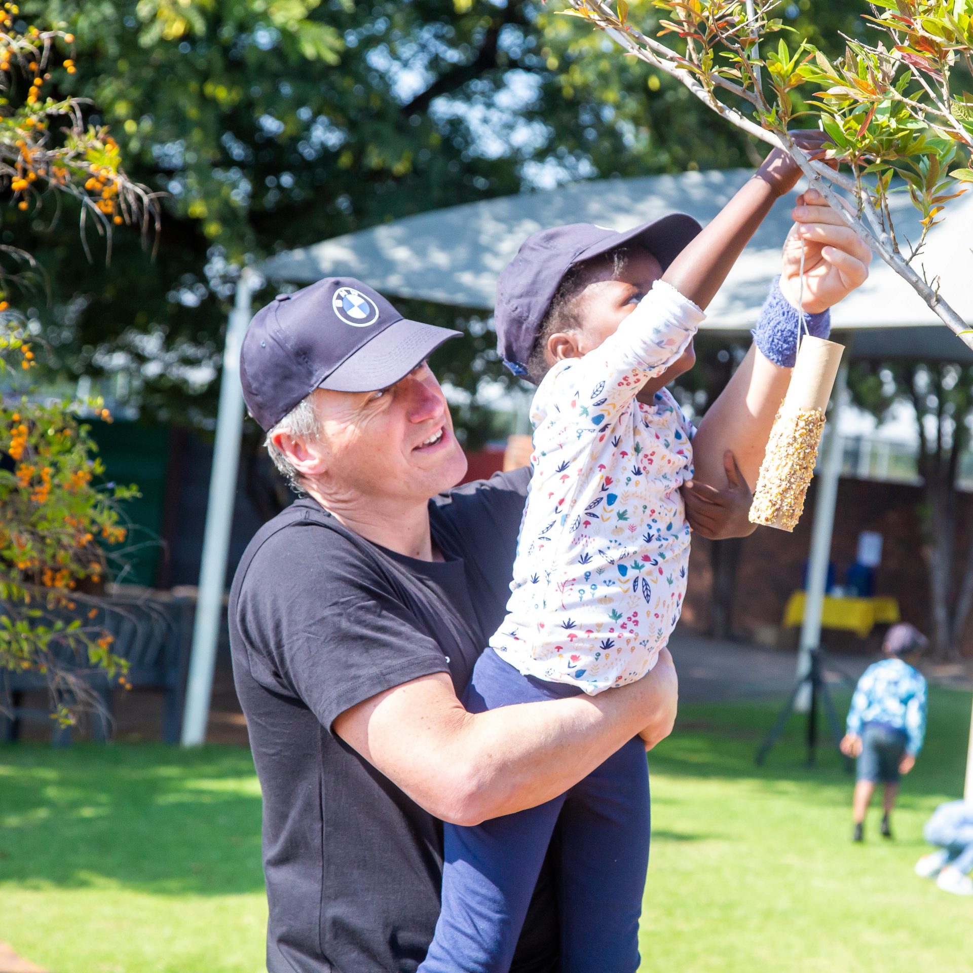 BMW Group South Africa employee holding a young child up to hang up a bird feeder.