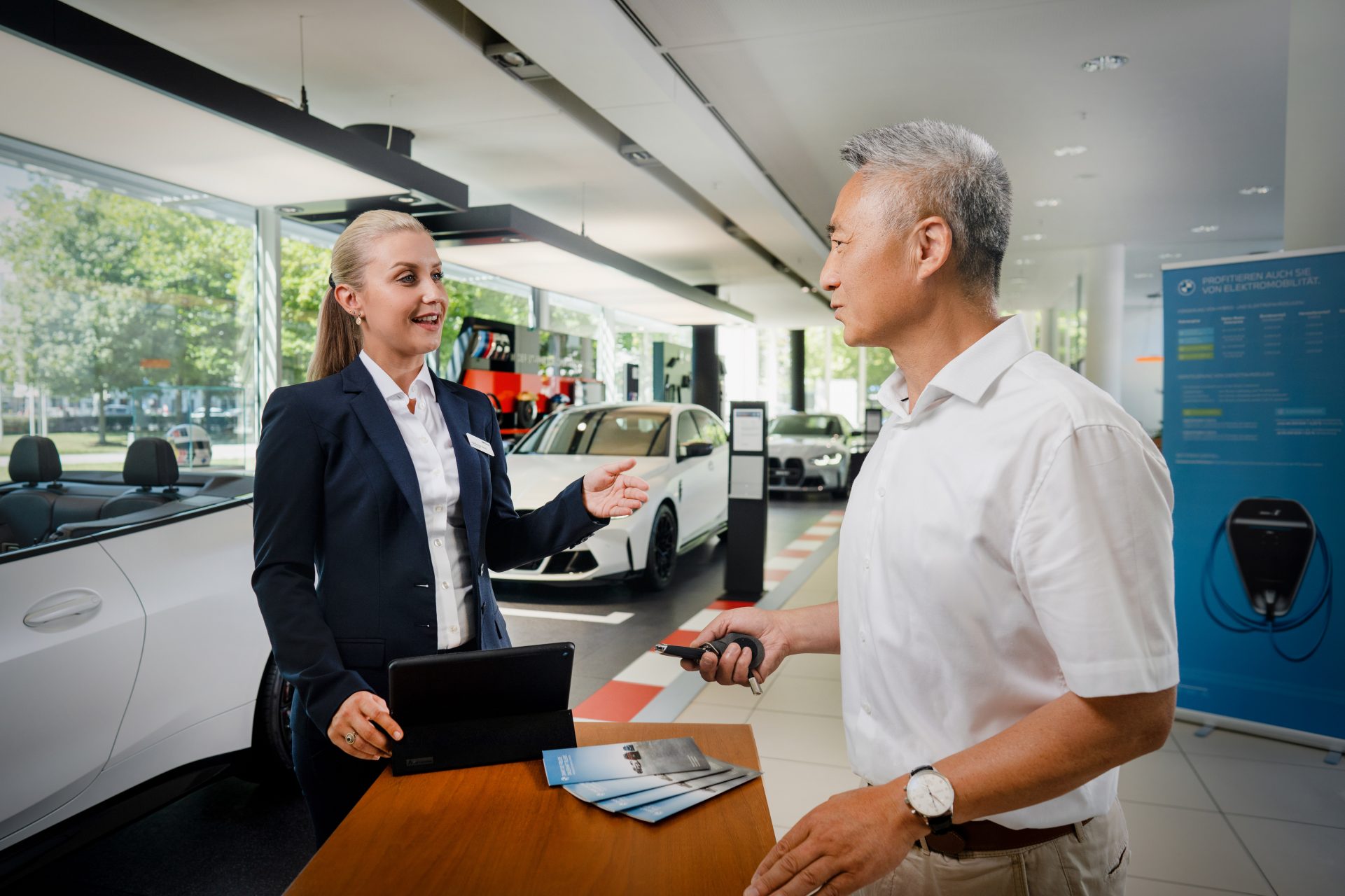 Un asistente de gestión de ventas de automóviles habla con un cliente en un concesionario BMW.