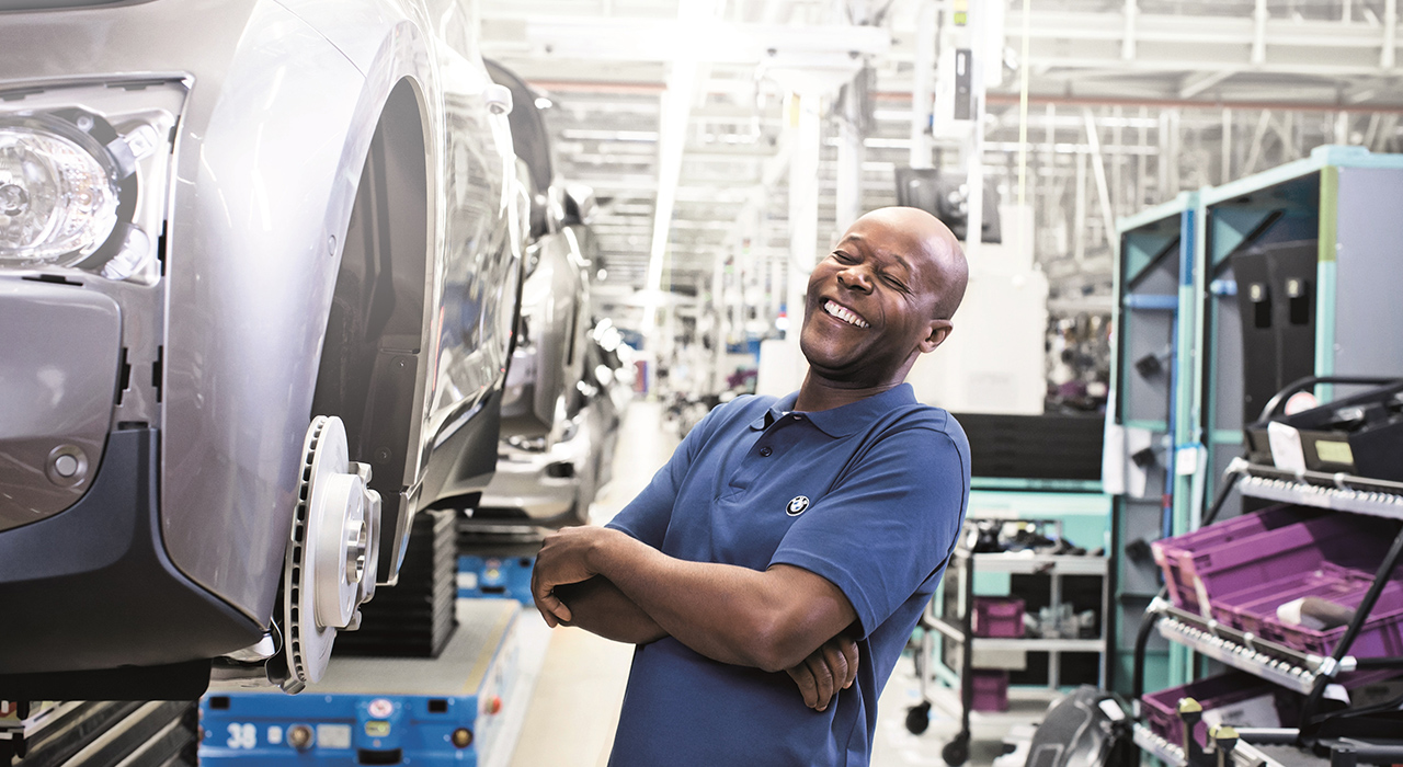 Das Bild zeigt einen lachenden Arbeiter in der Produktion bei BMW.
