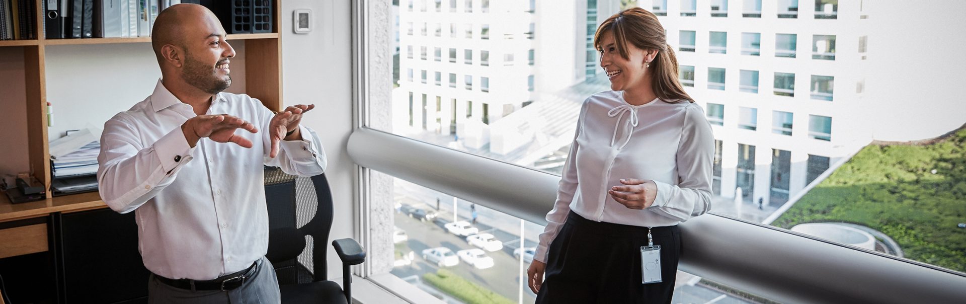 Zwei lachende BMW MItarbeitende im Gespräch in einer modernen Office Umgebung.
