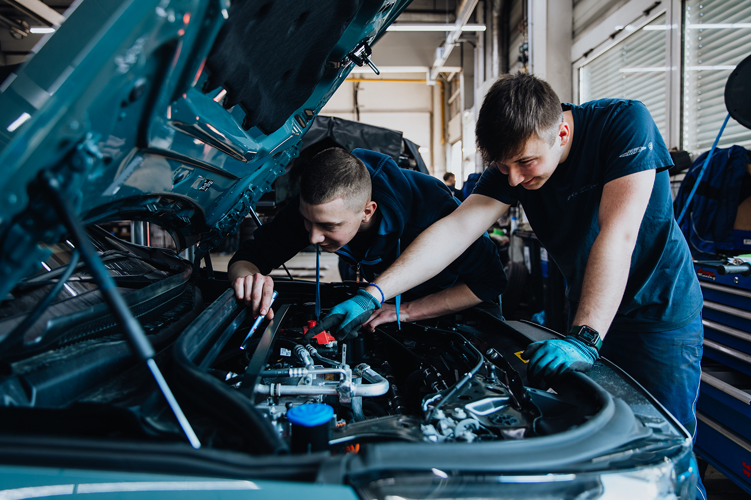 Zwei Azubis im Bereich Kfz-Mechatronik arbeiten am Motor eines Autos