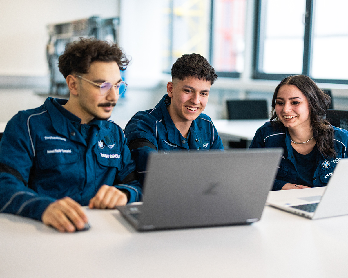 Drei Lehrlinge sitzen am Laptop und lachen-