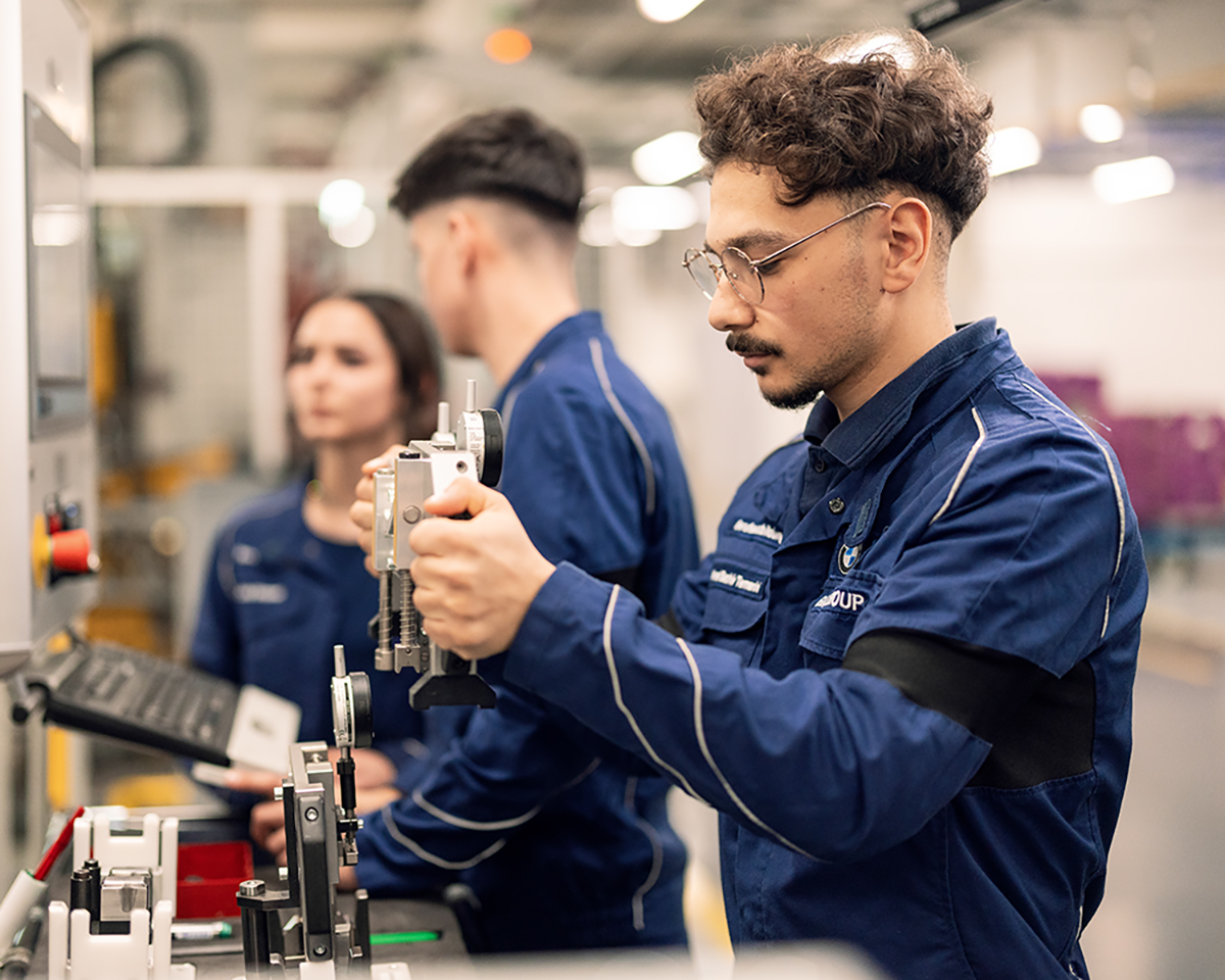 Drei Mitarbeitende arbeiten an einem Motoren Produktionsband.