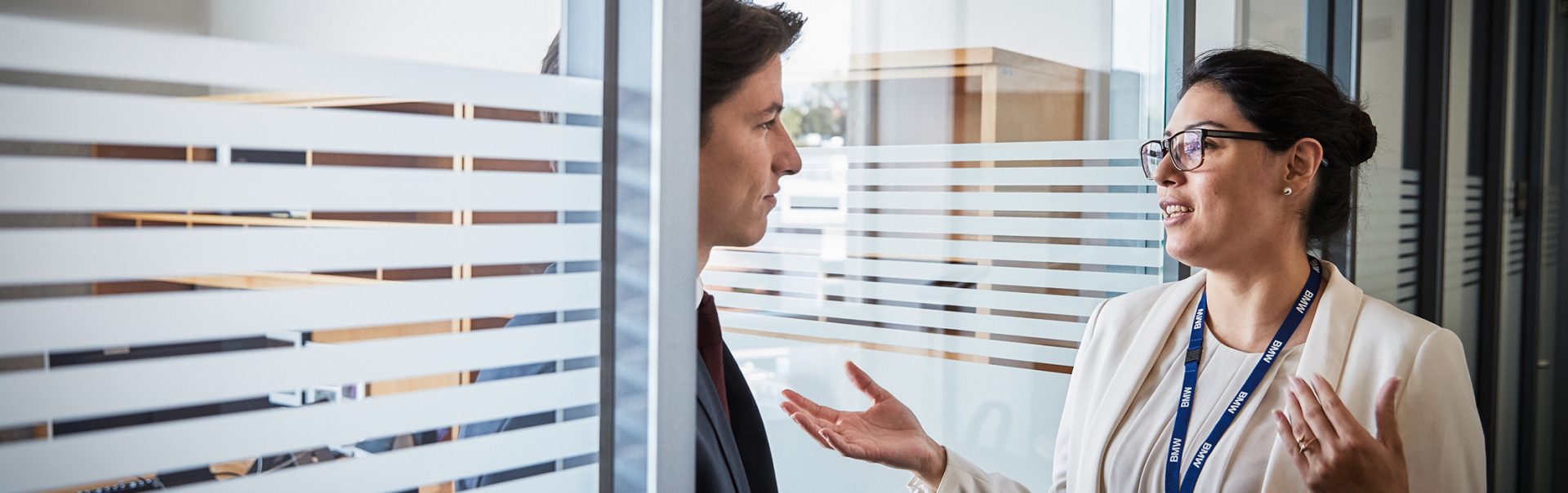 Two colleagues have a chat infornt of a class window.