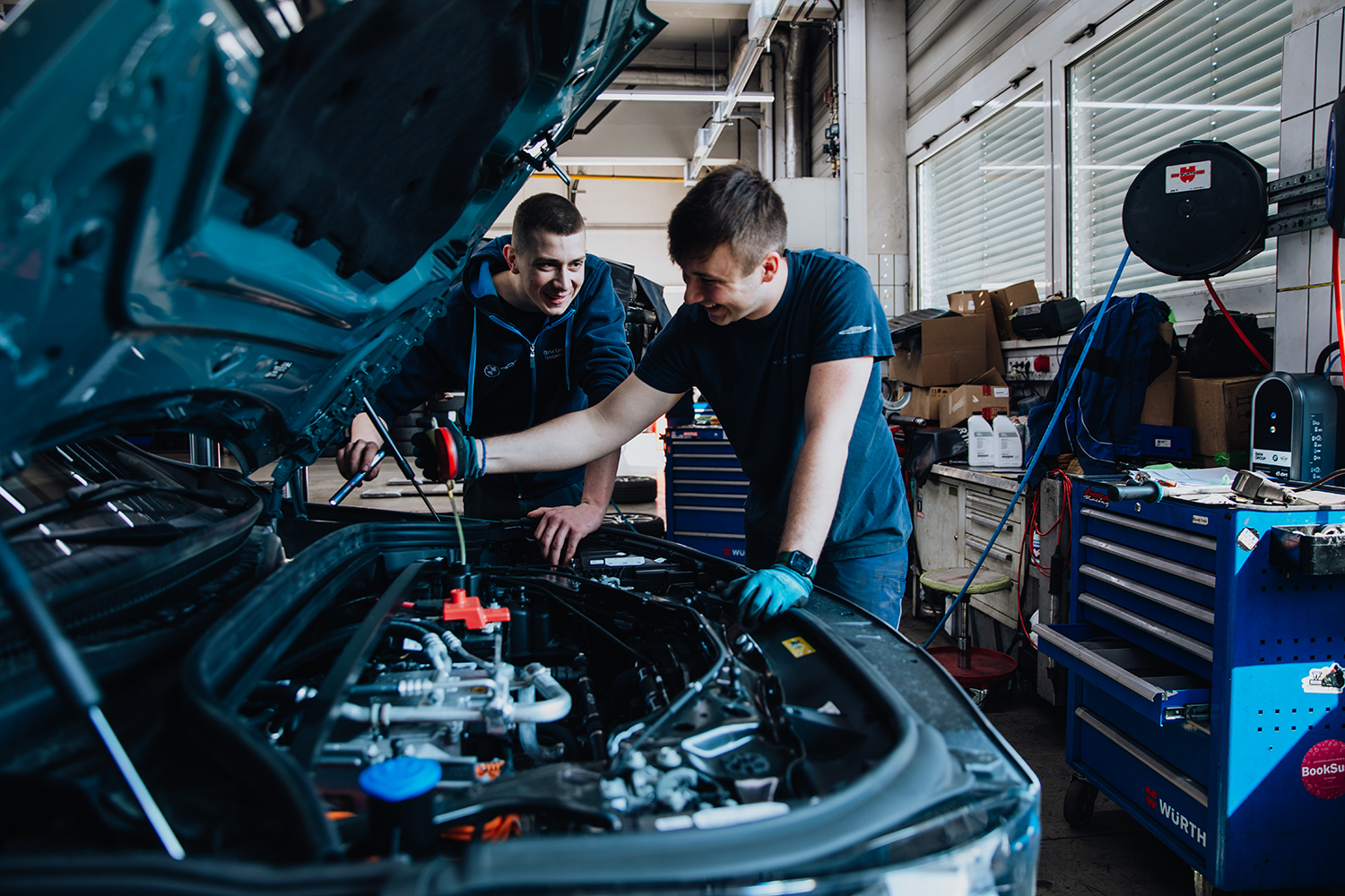 Zwei Kfz-Mechatronik-Azubis arbeiten an einer geöffneten Motorhaube