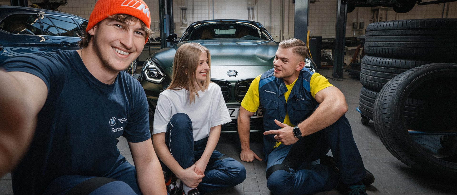 Drei Azubis unterhalten sich vor einem BMW Z4 in der Werkstatt