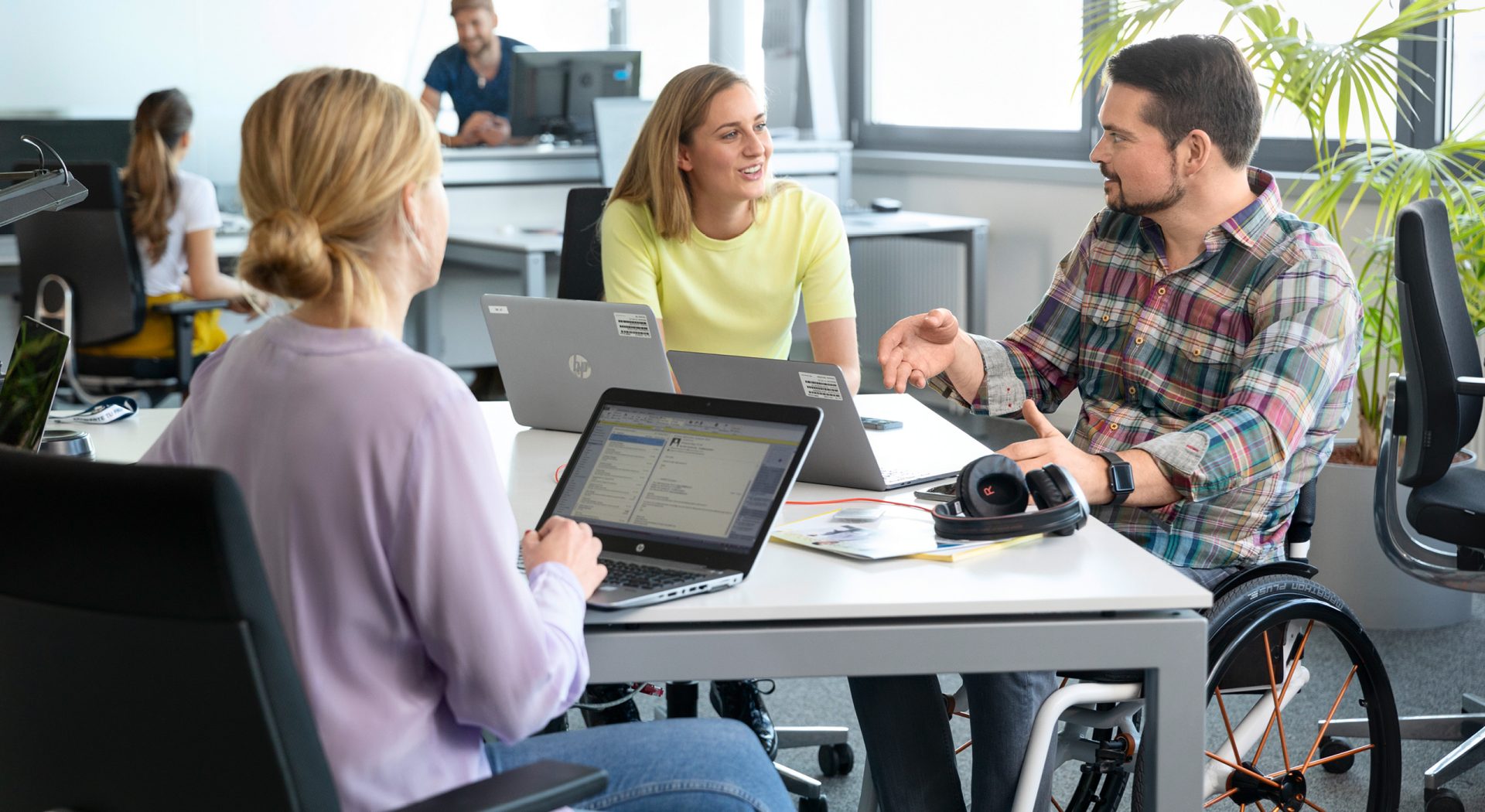 The picture shows three colleagues in a meeting, one of them sitting in a wheelchair.
