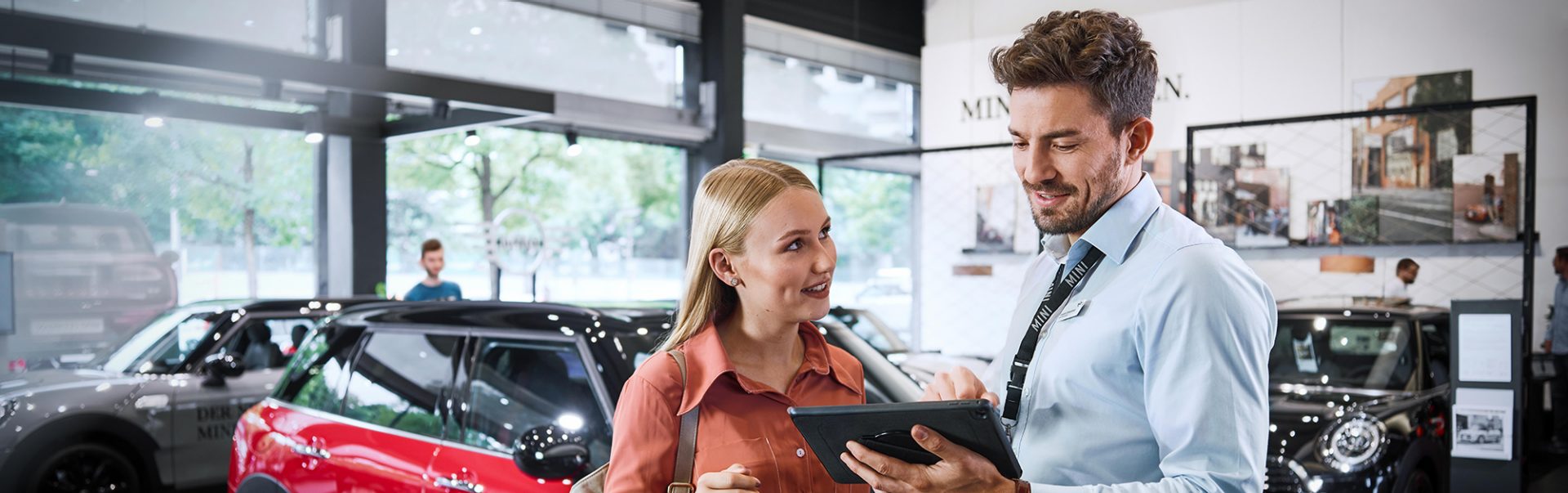 We see two young BMW employees having an animated conversation in a modern car dealership.