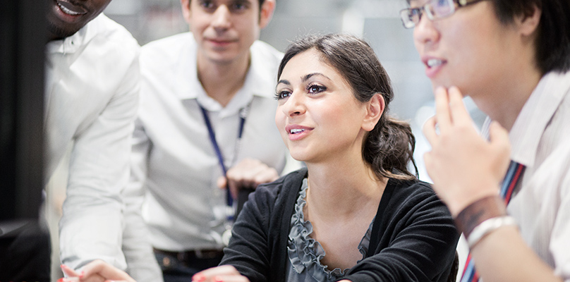 Three male students and a female student are looking at a computer.