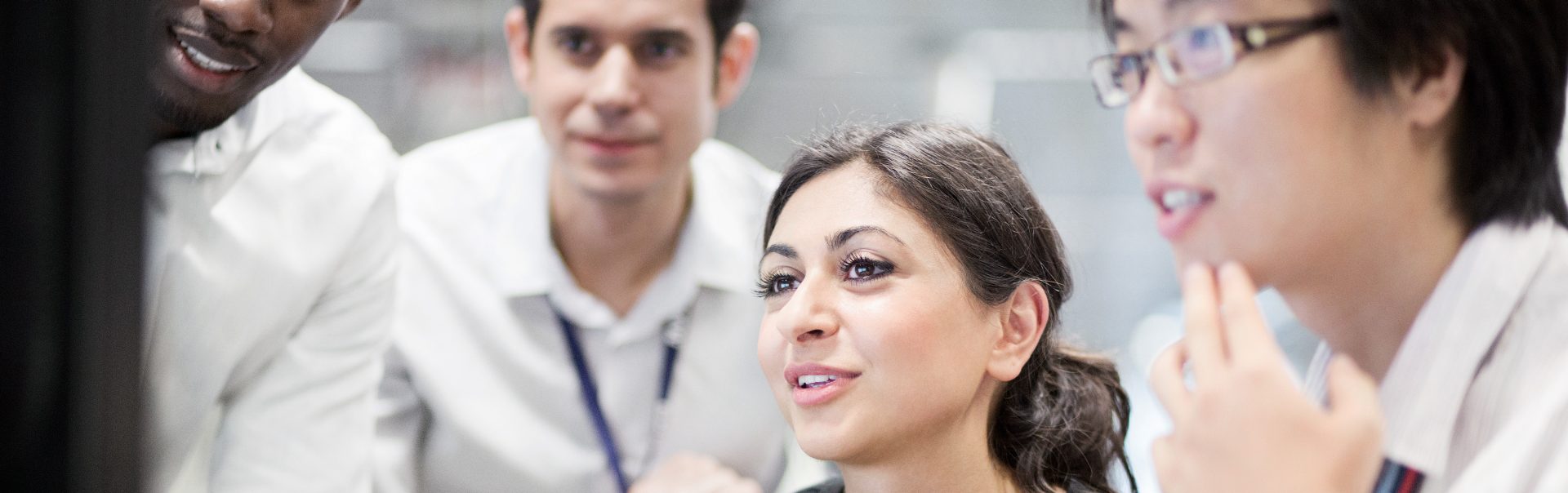 Três estudantes do sexo masculino e uma estudante estão olhando para um computador.