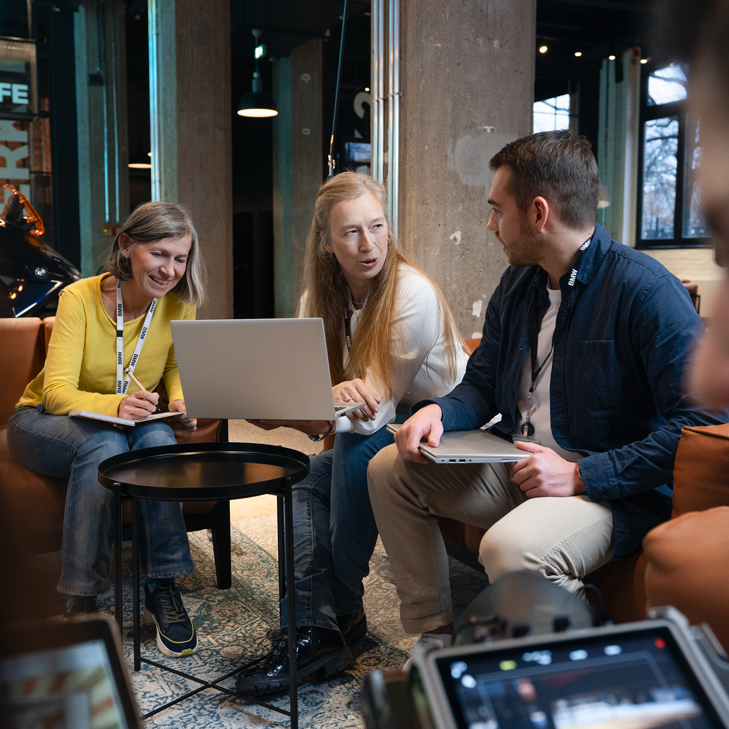 Drei Kolleg:innen in einer Besprechung mit Laptops auf dem Sofa