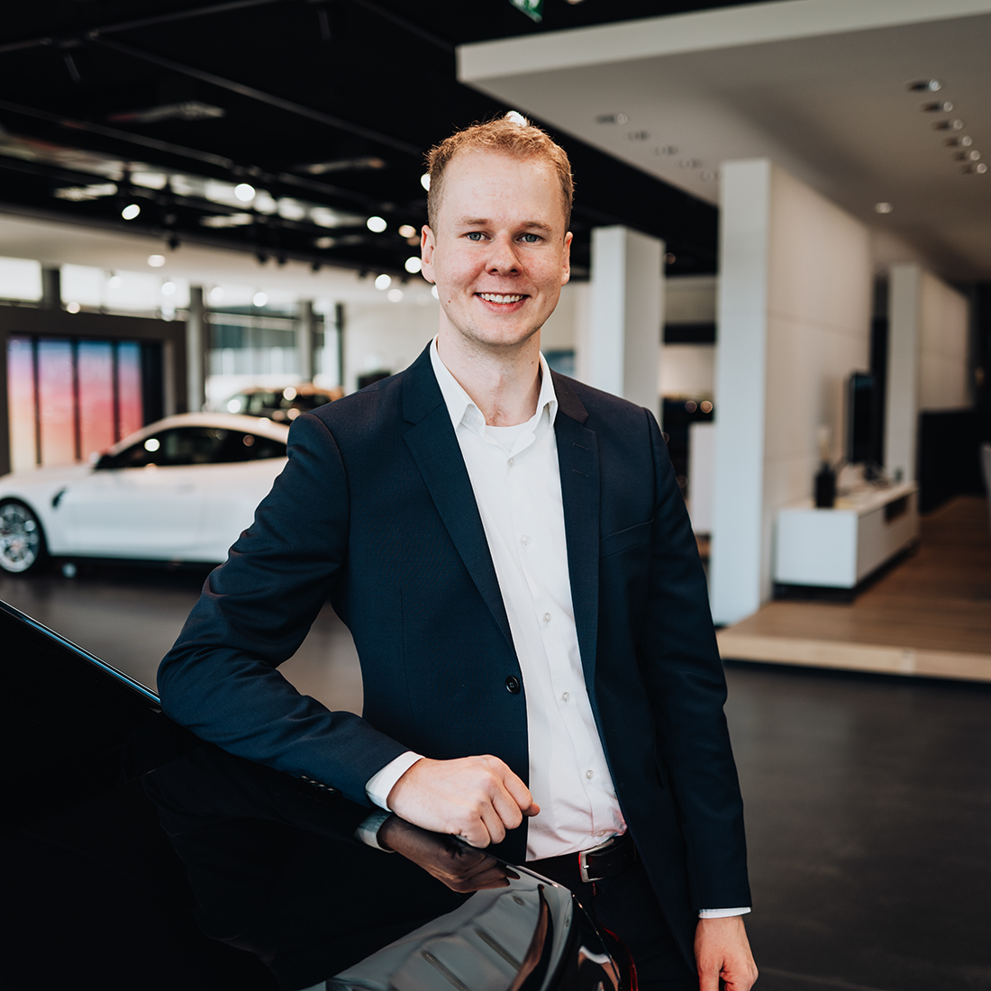 BMW Mitarbeiter Marcel lehnt am Kofferraum eines Autos