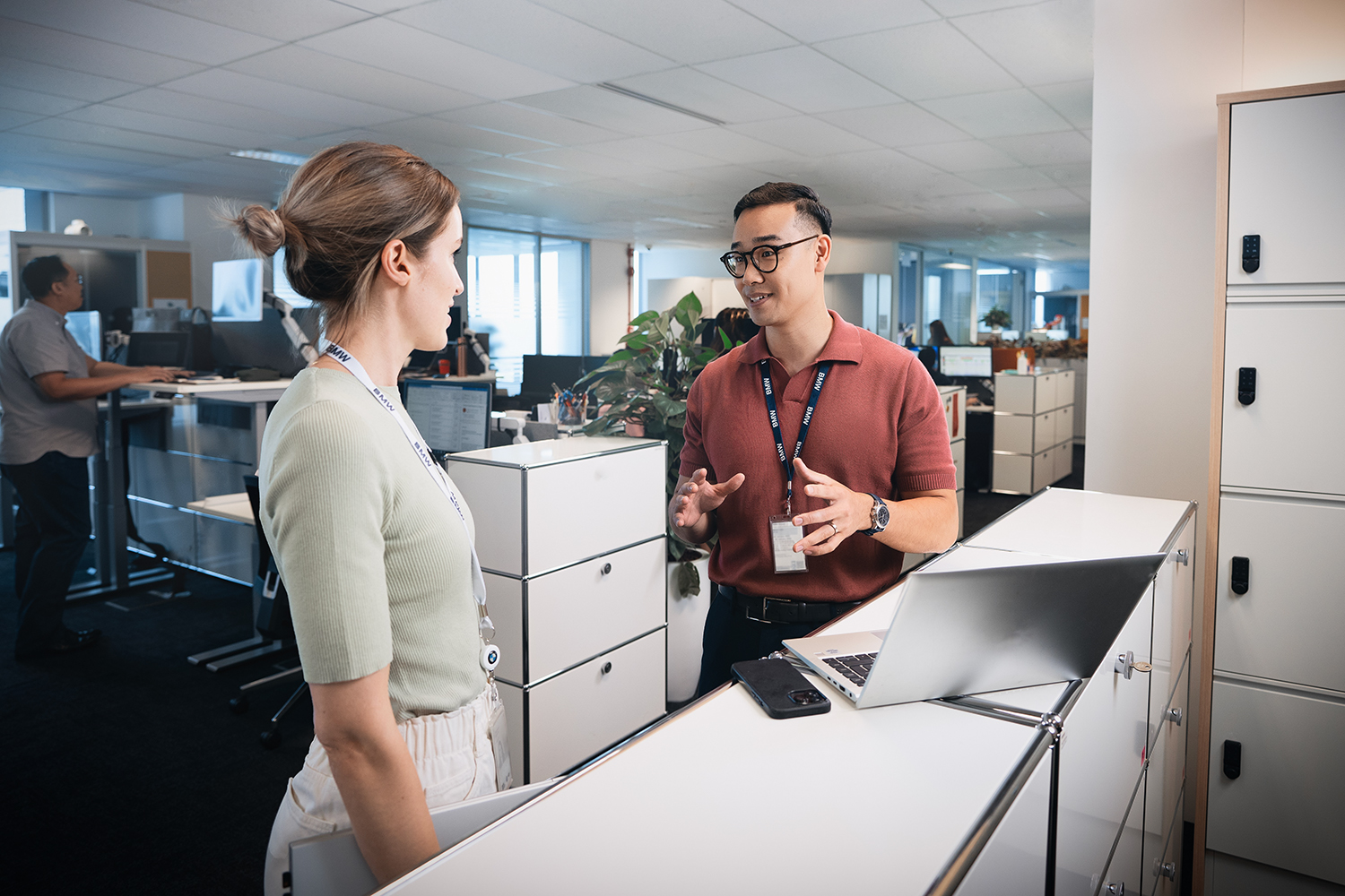 Eine Mitarbeiterin unterhält sich mit einem Praktikanten an einem Sideboard