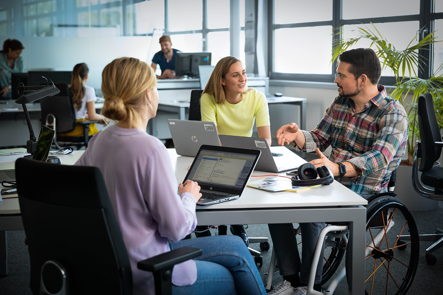 Drei Kolleg:innen, einer davon im Rollstuhl, bei einer Besprechung im Büro