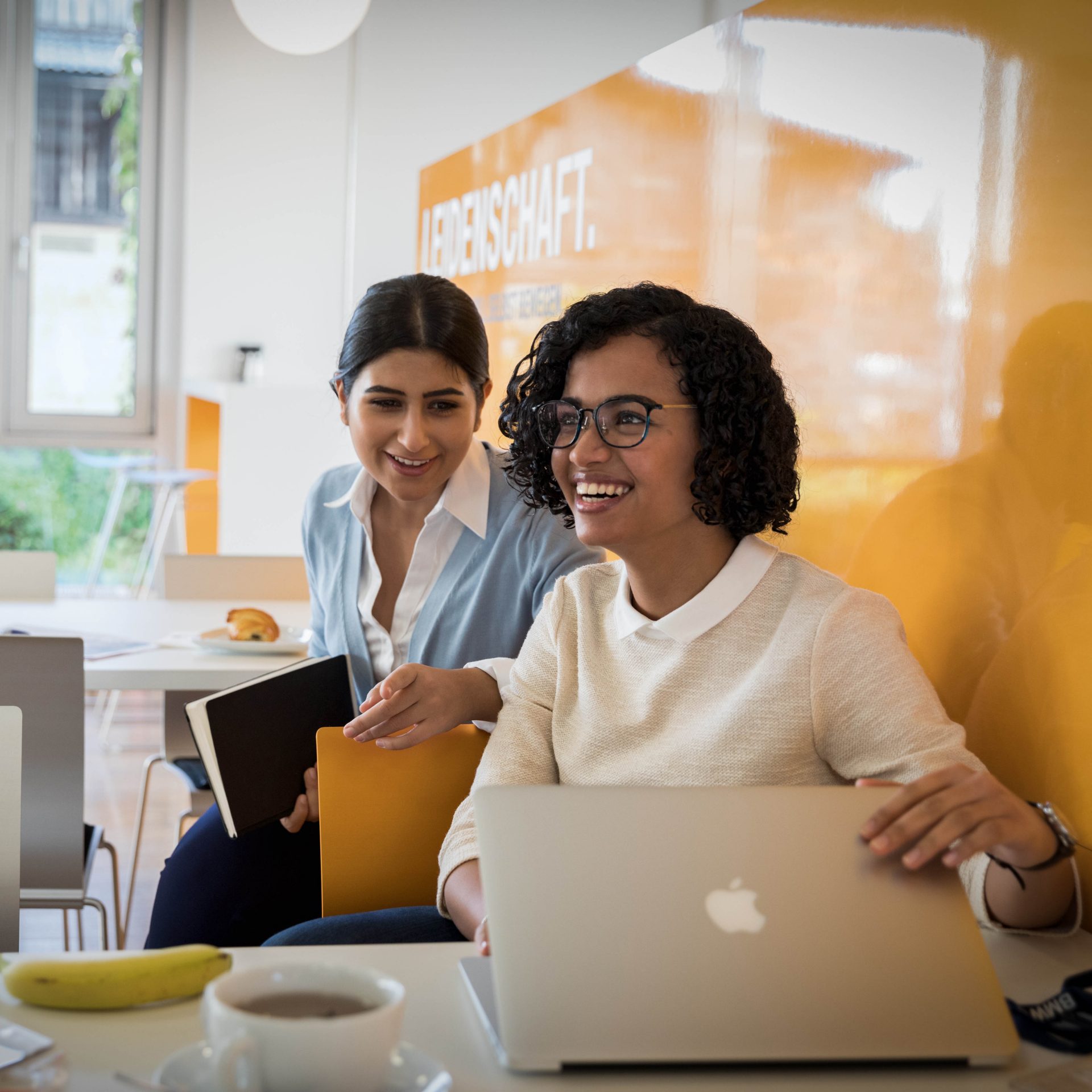 Two female colleagues are having a chat in the cafeteria.