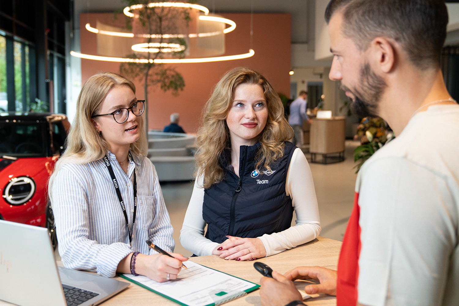 Two apprentices are having a conversation with a costumer in a MINI dealership.