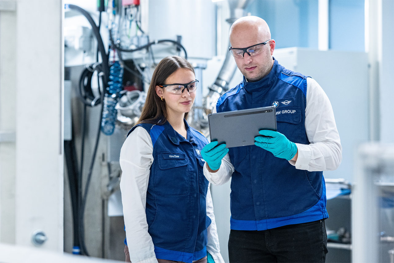 Zwei Mitarbeitende der BMW Group analysieren KI-gestützte Daten aus der Batteriezellfertigung auf einem Tablet.