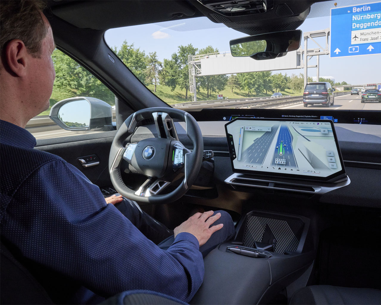 A BMW iX3 on the motorway: With the motorway assistant activated, drivers can simply rest their hands in their laps. The central display shows the active navigation and driver assistance.