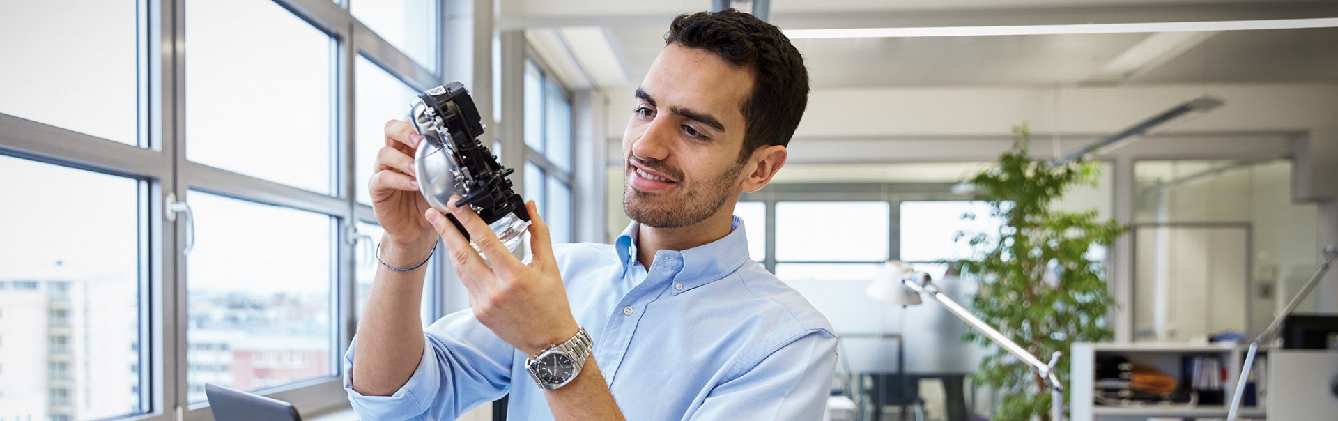 The picture shows a young man sitting in front of a laptop, inspecting a car part.