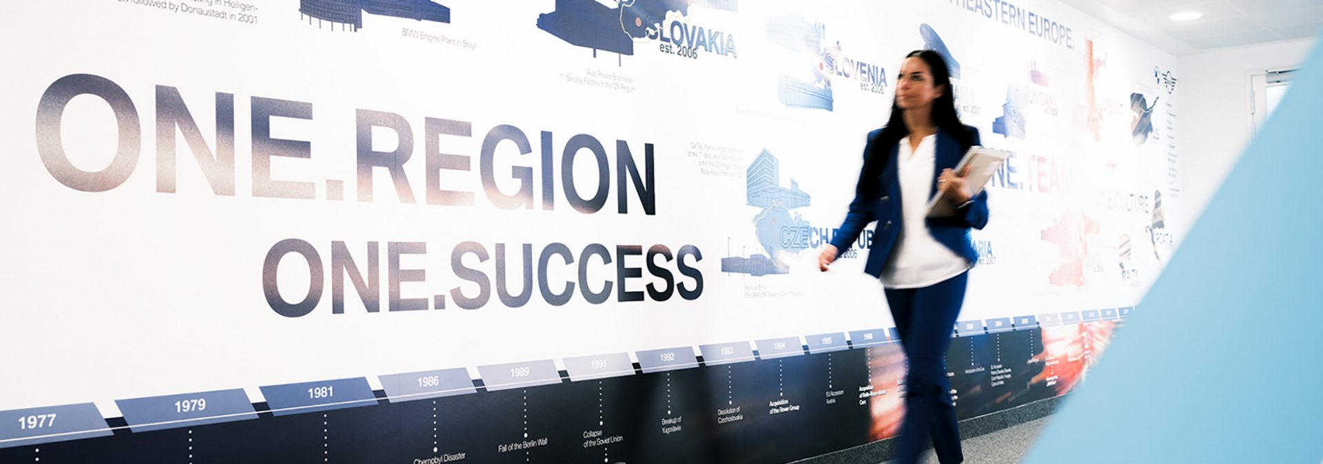 Women walking in front of a wall with the sign "One Region. Once Success."