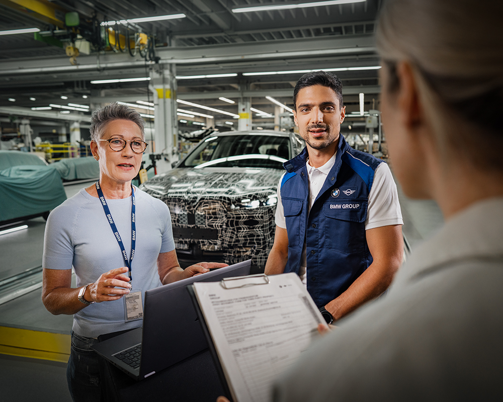 Drei Ingenieure von BMW in der Produktionslinie mit einem BMW Fahrzeug im Hintergrund.