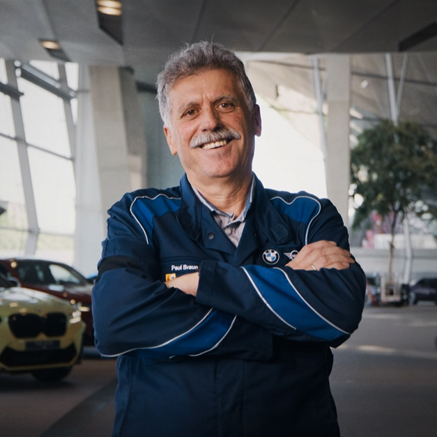 BMW Mitarbeiter Paul mit verschränkten Armen lachend in der BMW Welt