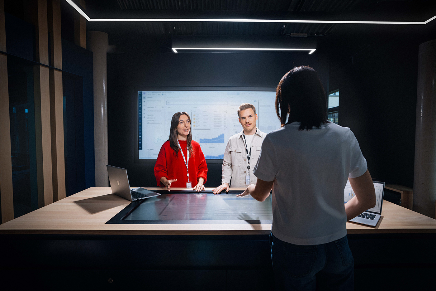 Drei IT-Kolleg:innen bei einer Unterhaltung an einem interaktiven Tisch
