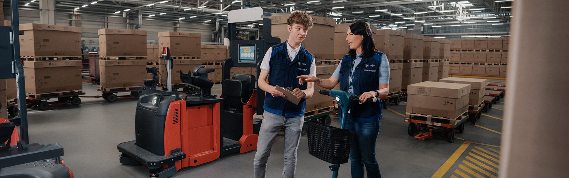 Zwei Lagerarbeiter bei BMW Logistik im Lager mit einem elektrischen Transportgerät.