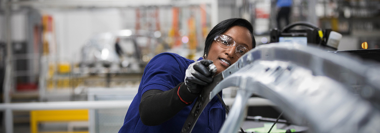 Eine junge Frau arbeitet an einer BMW Karosserie.