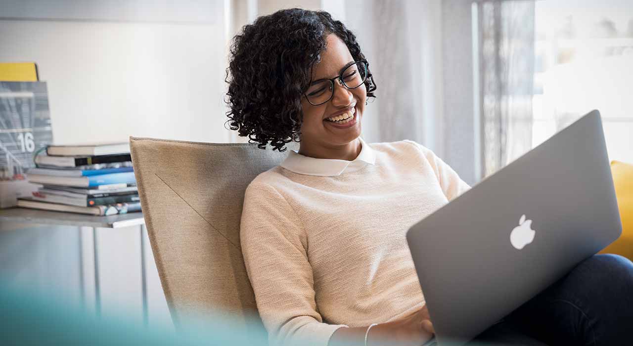 Das Bild zeigt eine Frau die lachend an ihrem Laptop sitzt.