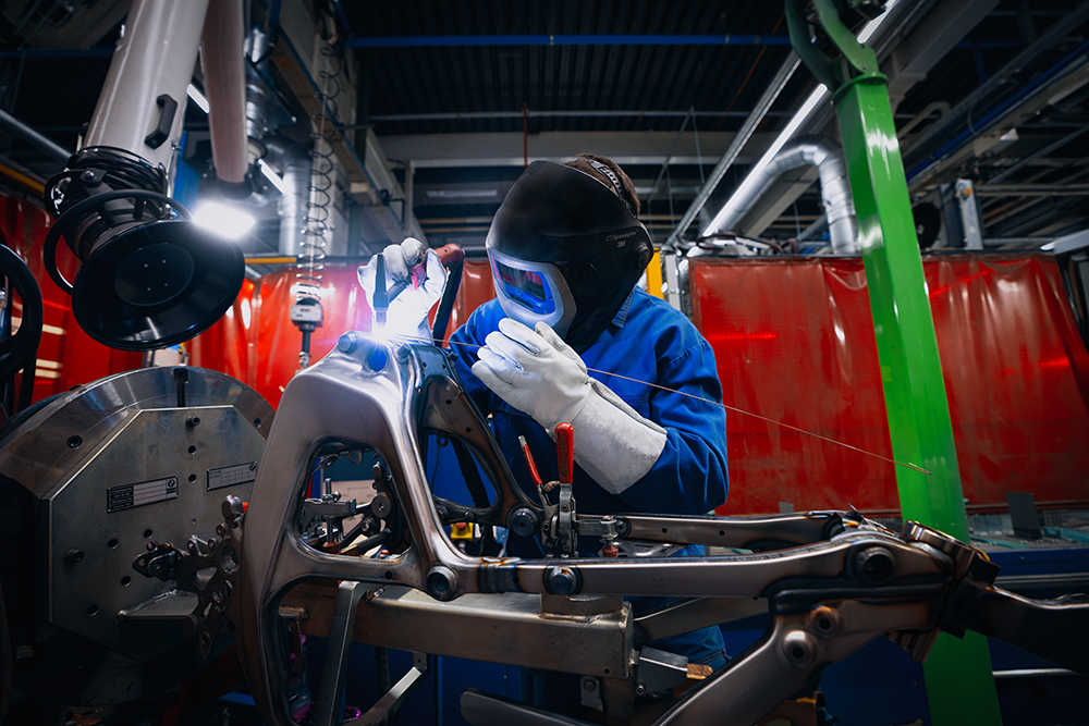 Nahaufnahme eines Mitarbeiters der BMW Group, der Motorradteile schweißt.