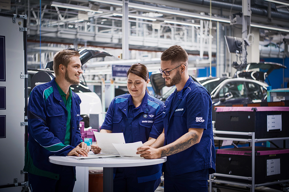 Three BMW professionals are meeting at the assembly line.