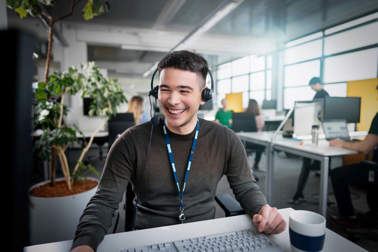 Freundlicher Kundenservice-Mitarbeiter mit Headset in einem modernen Büro bei der BMW Group.