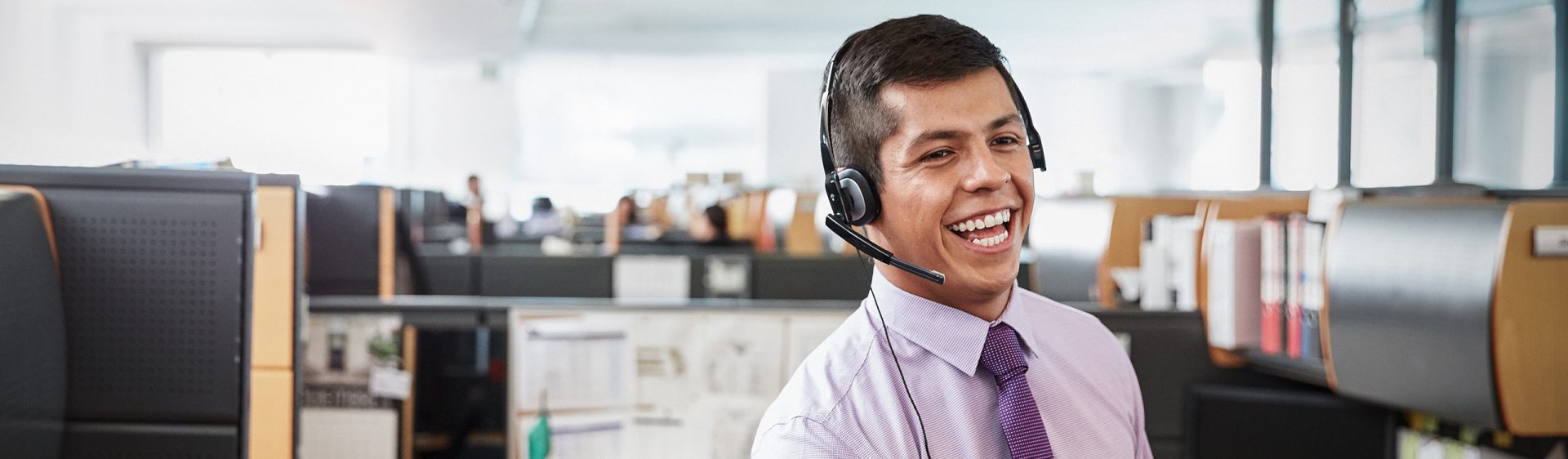Das Bild zeigt einen jungen Mann, der in der Kundenbetreuung arbeitet, in einem Büro sitzt und ein Headset trägt.