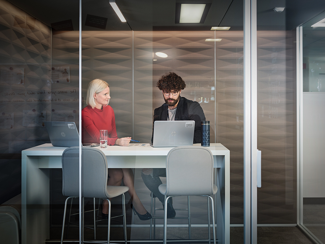 Teamarbeit zwischen einer Frau und einem Mann in einem Besprechungsraum mit Glaswänden.