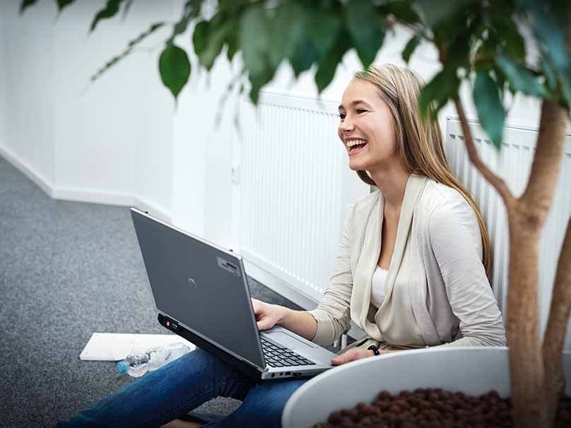 Eine junge Auszubildende der BMW Group sitzt lachend mit ihrem LapTop auf dem Boden.