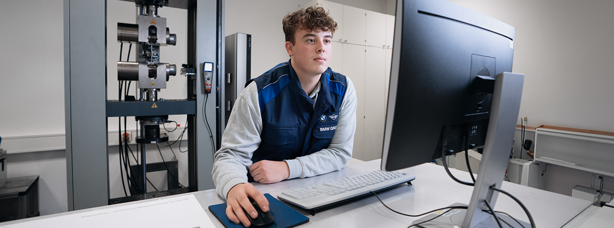 Ein Auszubildender steht an einem Schreibtisch und blickt konzentriert auf den Monitor.