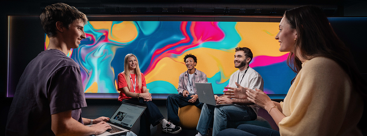 Fünf Auszubildende sitzen im Kreis und diskutieren vor einem bunten Hintergrund.