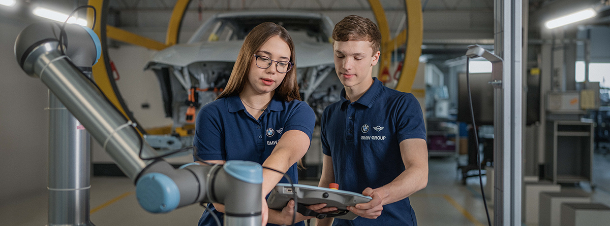 Zwei Studierende bei der BMW Group besprechen Daten auf einem Tablet in einer Produktionsumgebung.